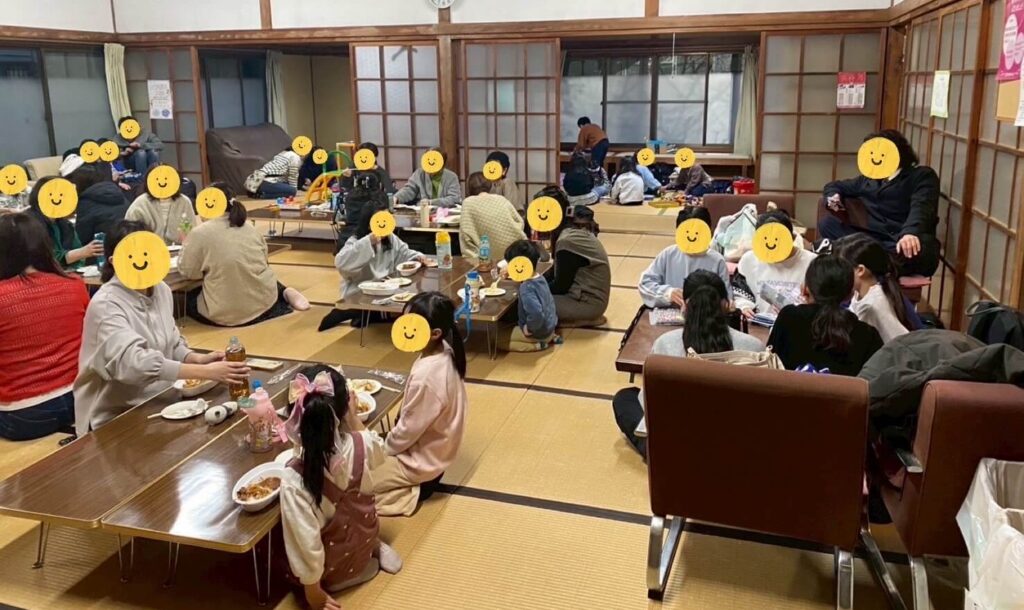 徳島県で開催されているたみやニコニコ子ども食堂の会場全体の様子。テーブルを囲む子どもや保護者が明るい室内で食事や交流を楽しんでいる風景。